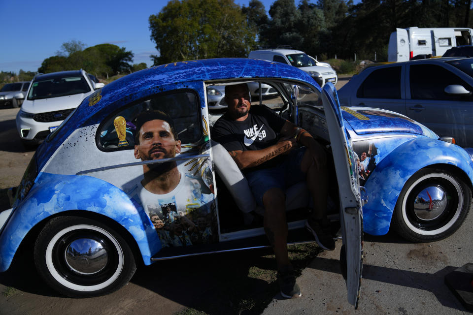 A soccer fan sits in a Volkswagen beetle emblazoned with the image of Argentina soccer star Lionel Messi, outside the Argentina Soccer Association facilities prior to a training session in preparation for a friendly soccer match between Argentina and Panama, in Buenos Aires, Argentina, Wednesday, March 22, 2023. (AP Photo/Natacha Pisarenko)