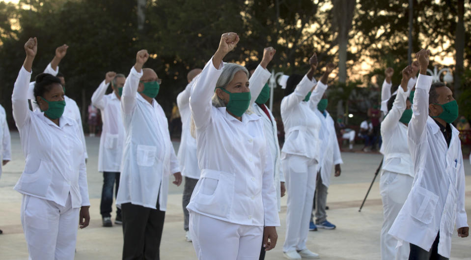 Una brigada de profesionales de la salud cubanos, que se ofrecieron como voluntarios para viajar a las Indias Occidentales, levantan el puño derecho mientras cantan el himno nacional de su país, en La Habana, Cuba, el sábado 28 de marzo de 2020. (AP Foto / Ismael Francisco)