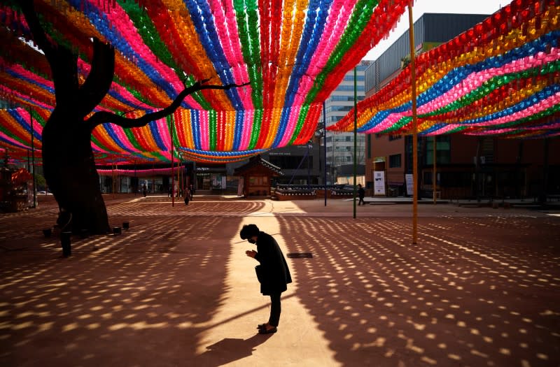 Buddhist believer wearing a face mask to prevent contracting the coronavirus disease (COVID-19) prays under colorful lanterns in preparation of the upcoming birthday of Buddha at a temple in Seoul,