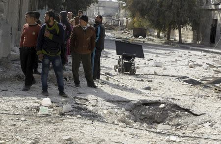 Men stand near a hole in the ground as they inspect the damage after airstrikes by pro-Syrian government forces in the rebel held al-Sakhour neighbourhood of Aleppo, Syria February 5, 2016. REUTERS/Abdalrhman Ismail