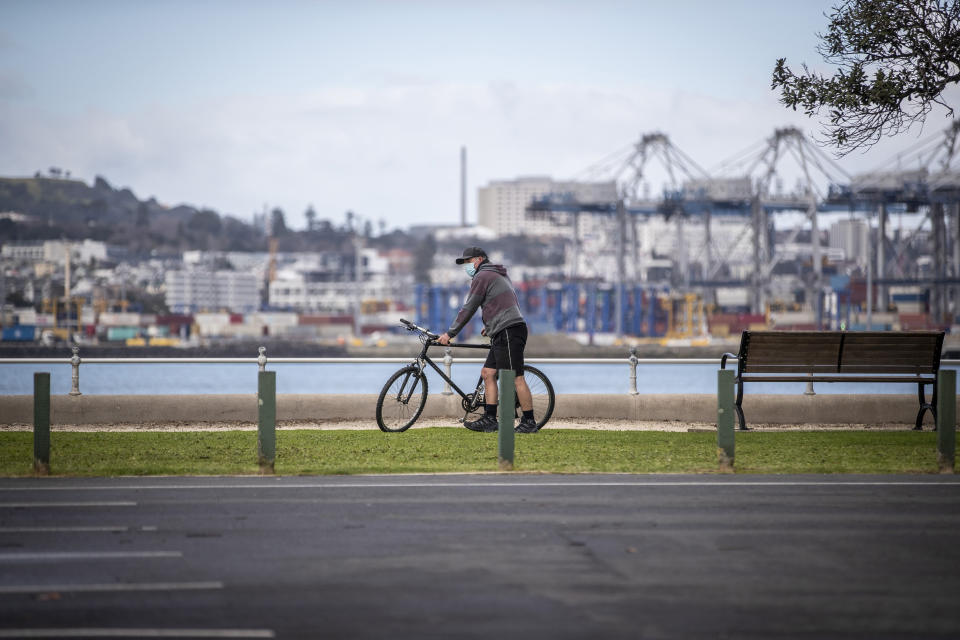 A cyclist wearing a mask pauses along the waterfront in Auckland, New Zealand, on Thursday, Aug. 19, 2021. Japan, Australia and New Zealand all got through the first year of the coronavirus pandemic in relatively good shape, but now are taking diverging paths in dealing with new outbreaks of the fast-spreading delta variant. (Michael Craig/New Zealand Herald via AP)