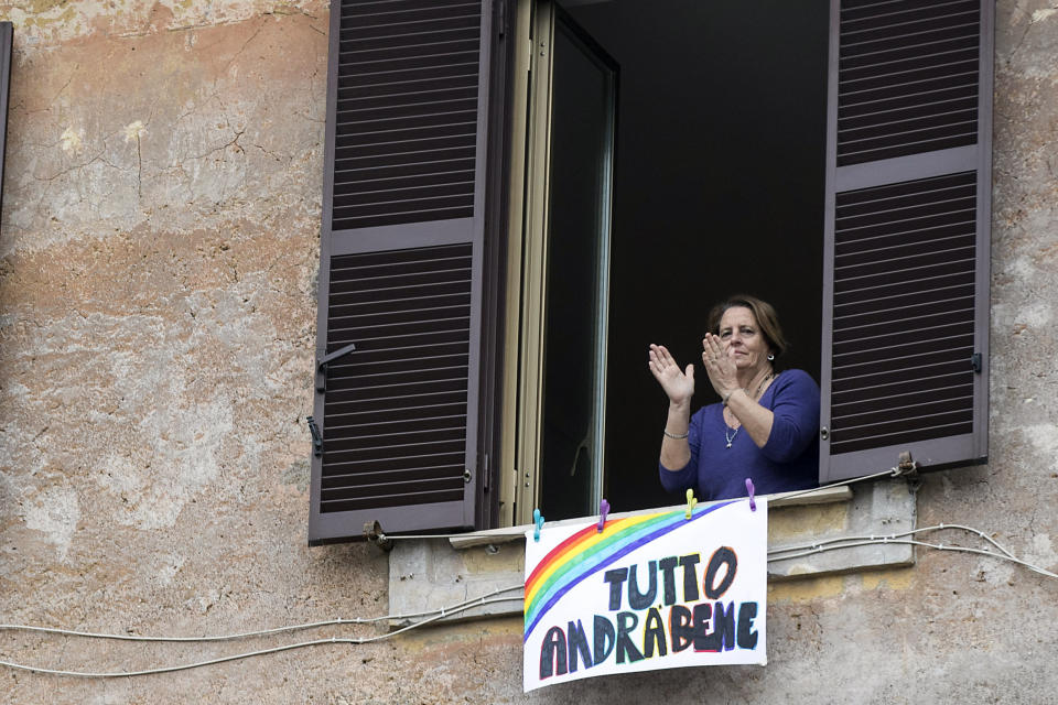 In this photo taken on Saturday, March 14, 2020, a woman claps her hands next to a banner reading "Everything will be alright", in Rome. The nationwide lockdown to slow coronavirus is still early days for much of Italy, but Italians are already are showing signs of solidarity. This week, children’s drawings of rainbows are appearing all over social media as well as on balconies and windows in major cities ready, ‘’Andra’ tutto bene,’’ Italian for ‘’Everything will be alright.’’ For most people, the new coronavirus causes only mild or moderate symptoms. For some, it can cause more severe illness, especially in older adults and people with existing health problems. (Roberto Monaldo/LaPresse via AP)