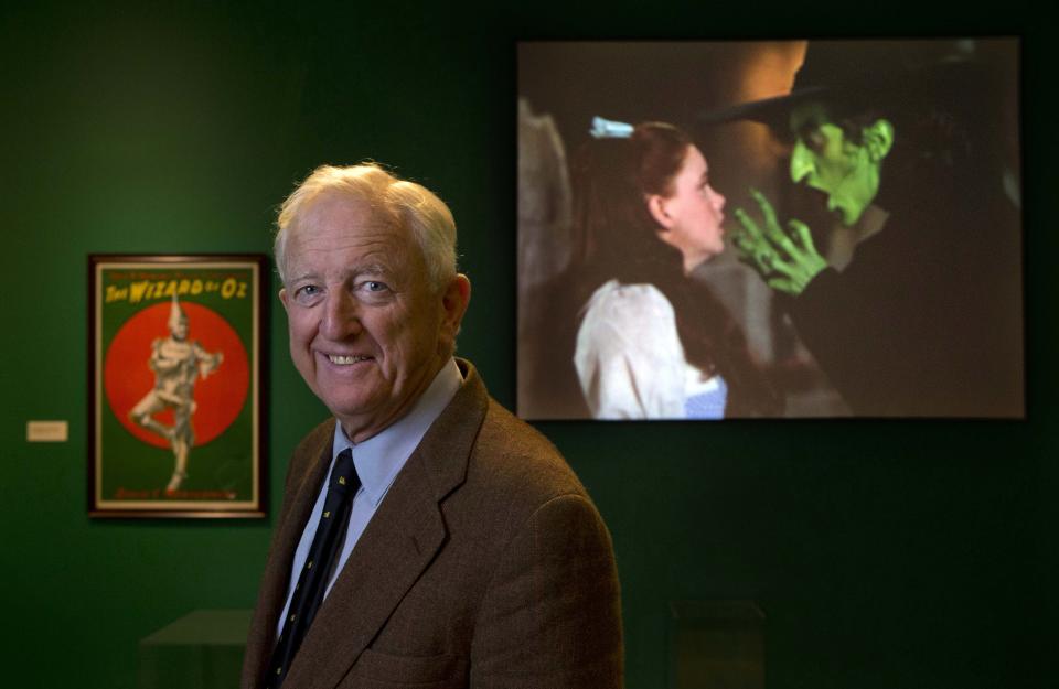 In this Tuesday, Oct. 8, 2013 photo, Ham Meserve, of Southport, Maine, the son of actress Margaret Hamilton, poses at the Farnsworth Museum, in Rockland, Maine. Hamilton is seen on the screen at right playing the role of the wicked witch of the West in the movie, "The Wizard of Oz." The world's largest collection of materials from the movie is being exhibited a few months after the release of a prequel to the original film and the release of the original movie in I-Max format. (AP Photo/Robert F. Bukaty)