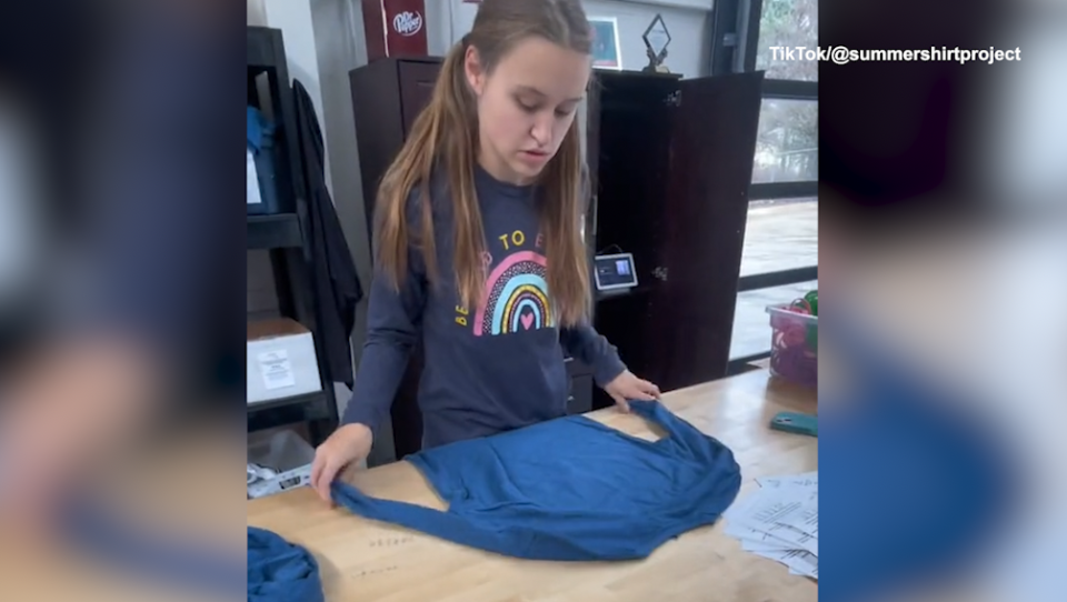 Jordyn rolls a shirt to ship out to a customer.  / Credit: Jordyn's Summer Shirt Project