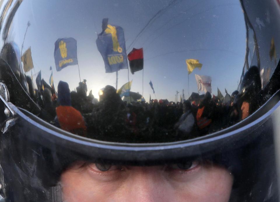 FILE - In this Sunday, Dec. 29, 2013 file photo a thousand-strong pro-European Union rally is reflected in the surface of a riot police officer's helmet as he guards the way to Ukrainian President Viktor Yanukovych?s country residence of Mezhygirya outside Kiev, Ukraine. After two months of anti-government protests, modern Ukraine has never been so bitterly polarized. To be sure, Ukraine has long been divided. Russia and Europe have vied for dominance for centuries, causing deep cultural differences between the mostly Ukrainian-speaking western and central regions on the one hand, and the Russian-speaking east and south on the other. But as the crisis has deepened, each side has grown stronger in its convictions, and those who stood in the middle have been forced to choose sides. (AP Photo/Efrem Lukatsky, File)