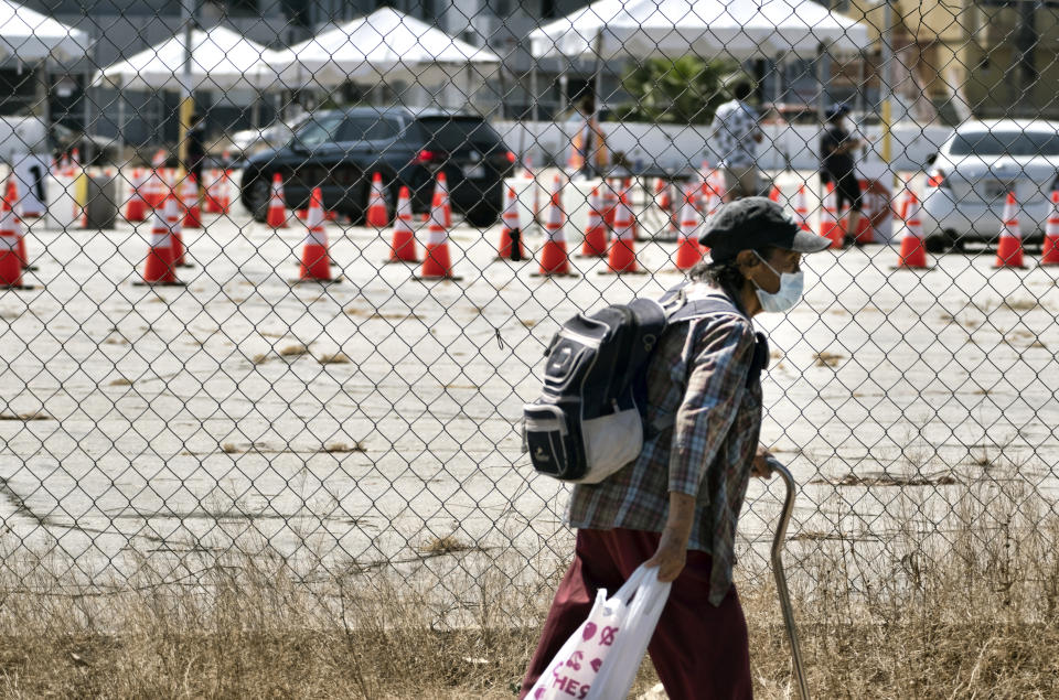 A masked pedestrian walks past a coronavirus testing site in the Panorama City section of Los Angeles on Tuesday, Aug. 3, 2020. A technical problem has caused a lag in California's tally of coronavirus test results, casting doubt on the accuracy of recent data showing improvements in the infection rate and hindering efforts to track the spread. (AP Photo/Richard Vogel)