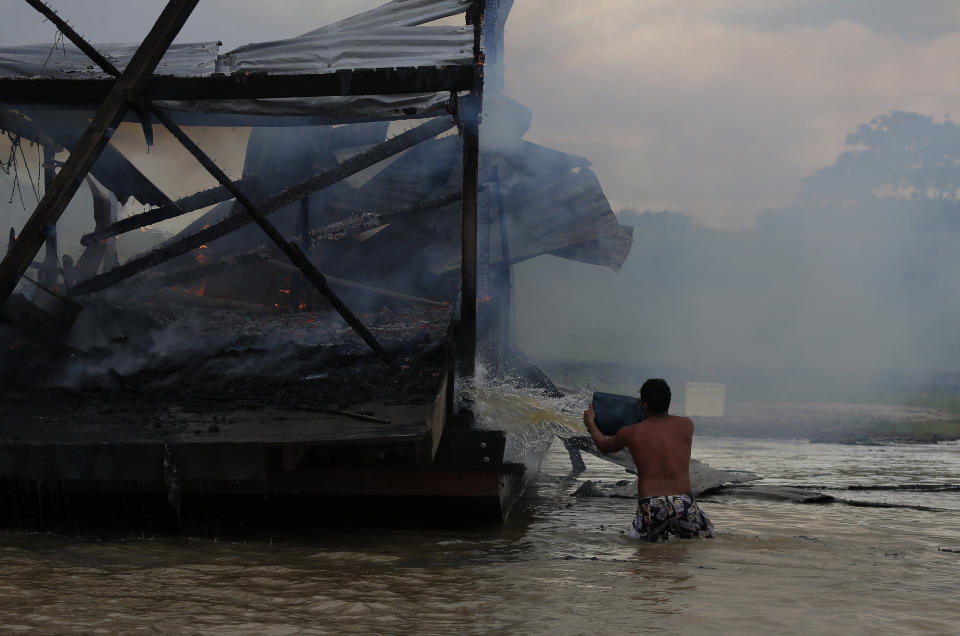 An illegal miner throws water at one of the more than 60 dredging barges that were set on fire by officers of the Brazilian Institute of the Environment and Renewable Natural Resources, IBAMA, during an operation to try to contain illegal gold mining on the Madeira river, a tributary of the Amazon river in Borba, Amazonas state, Brazil, Sunday, Nov. 28, 2021. Hundreds of barges belonging to illegal miners had converged on the river during a gold rush in the Brazilian Amazon prompting IBAMA authorities to start burning them. (AP Photo/Edmar Barros)