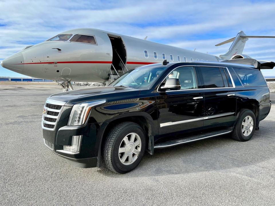 A car parked on a runway next to a VistaJet Bombardier Global 5000 private jet with its passenger loading door open.