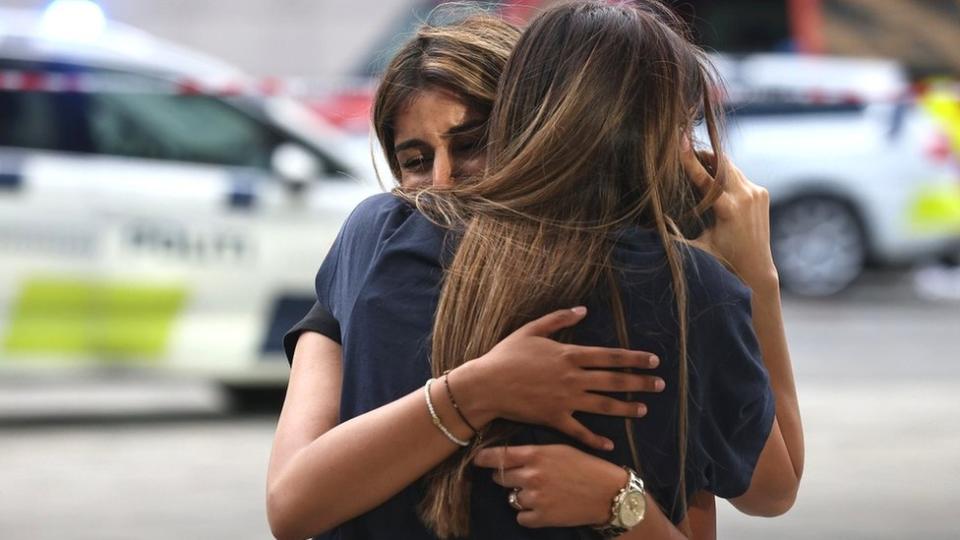 Two distressed women hug outside a Copenhagen shopping centre