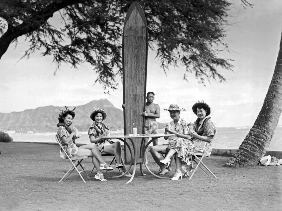 Four Japanese tourists pose at the Halekulani Hotel on Waikiki Beach with a native Hawaiian and his long surfboard, Honolulu, Hawaii, circa 1930.