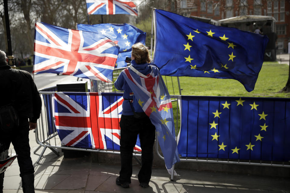 An anti-Brexit supporter stands by European and British Union flags placed opposite the Houses of Parliament in London, Monday, March 18, 2019. British Prime Minister Theresa May was making a last-minute push Monday to win support for her European Union divorce deal, warning opponents that failure to approve it would mean a long — and possibly indefinite — delay to Brexit. Parliament has rejected the agreement twice, but May aims to try a third time this week if she can persuade enough lawmakers to change their minds. (AP Photo/Matt Dunham)
