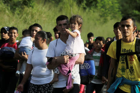 A man carries a child along other Hondurans fleeing poverty and violence, as they move in a caravan toward the United States, in San Pedro Sula, Honduras October 13, 2018. REUTERS/Jorge Cabrera