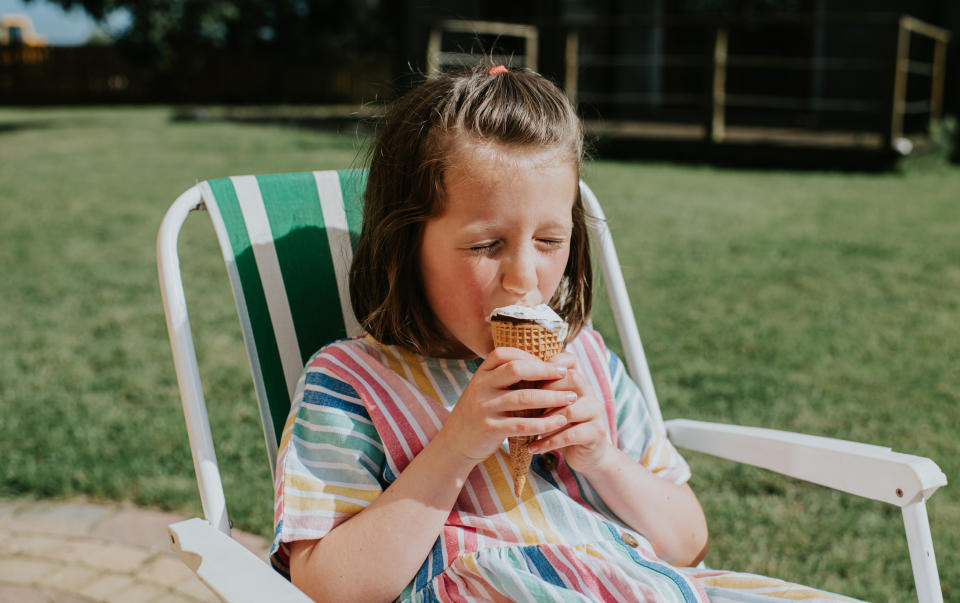 Child enjoys an ice cream cone while sitting in a sunny garden on a striped chair