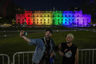 Rafael Teran, left, and his boyfriend Cristian Garcia, takes a selfie in front of the La Moneda presidential palace illuminated with rainbow colors, after lawmakers approved legislation legalizing marriage and adoption by same-sex couples, in Santiago, Chile, Tuesday, Dec. 7, 2021. (AP Photo/Esteban Felix)