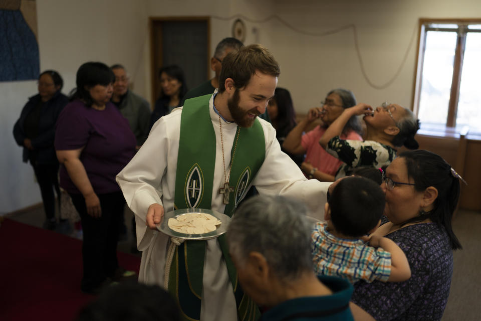 The Rev. Aaron Silco, center, who is a co-pastor of the Shishmaref Lutheran Church with his wife, Anna, gives Communion to church members during a Sunday service in Shishmaref, Alaska, Sunday, Oct. 2, 2022. They live next to the church and cemetery with their two-month-old son, Aidan. “There’s still life happening despite all of the weight and the burden that climate change can cast upon this community.” (AP Photo/Jae C. Hong)