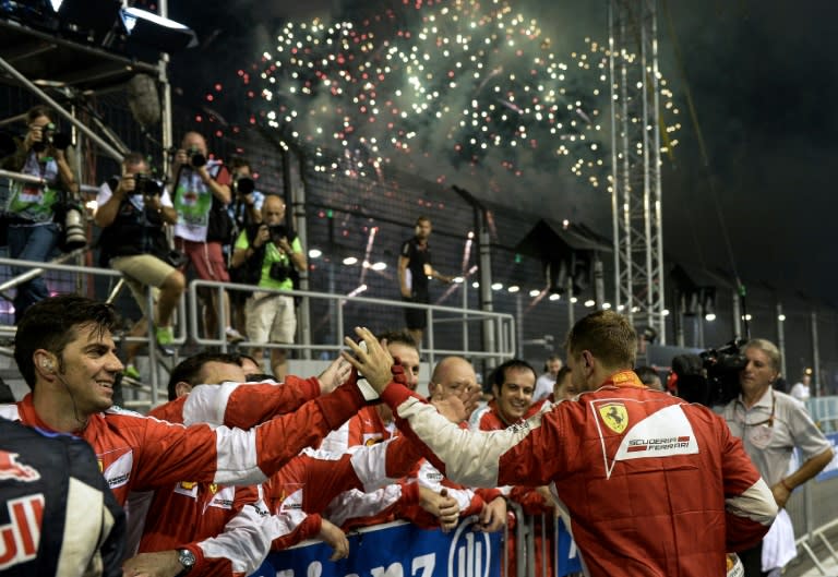 Ferrari's German driver Sebastian Vettel (R) celebrates his victory with team members as fireworks light up the sky after the Singapore Grand Prix on September 20, 2015