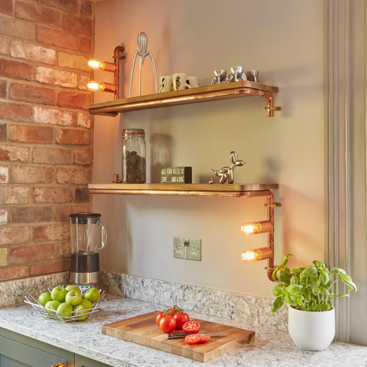  A kitchen with an exposed brick wall and copper lighting fixtures on the wall. 