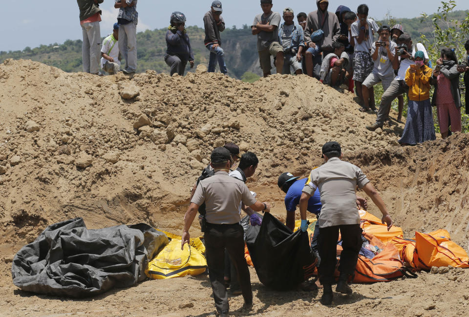 FILE - In this Monday, Oct. 12, 2018, file photo, rescue teams carry the bodies of victims to a mass grave following a major earthquake and tsunami in Palu, Central Sulawesi, Indonesia. Indonesia's disaster agency says helicopters are dropping disinfectant on neighborhoods in the earthquake and tsunami-stricken city of Palu to reduce disease risks from the thousands of victims believed buried in obliterated communities. (AP Photo/Tatan Syuflana, File)