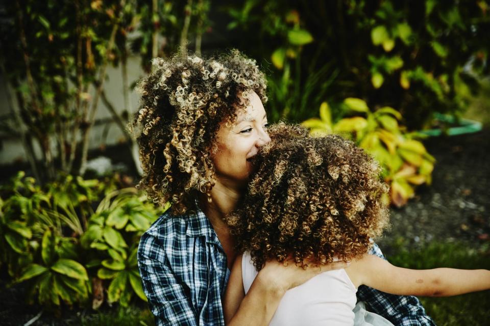 Mother holding daughter while sitting in yard