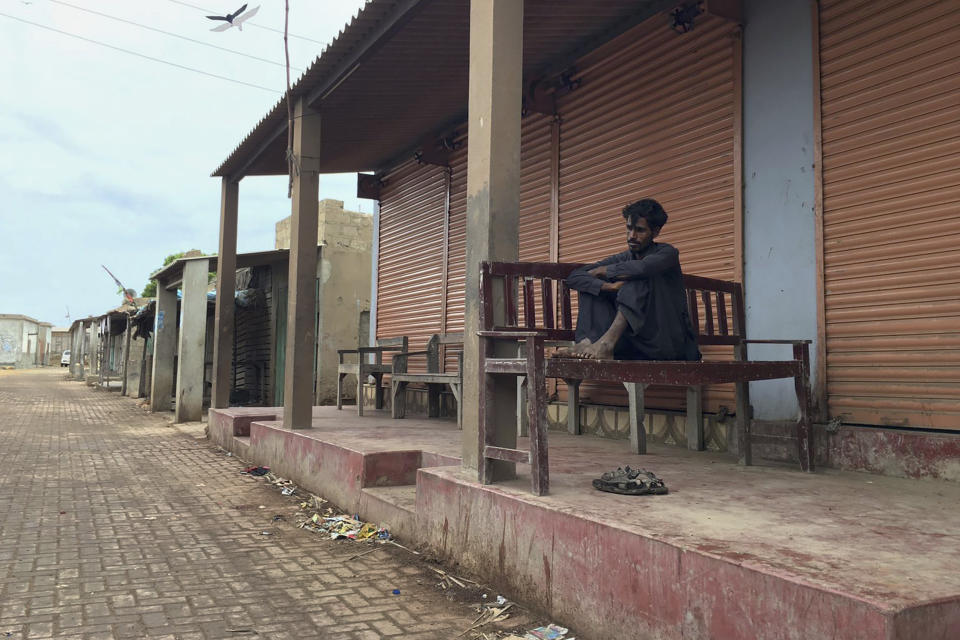 A local resident sits outside a closed shop in an empty market after people evacuated due to Cyclone Biparjoy approaching, at a costal area Keti Bandar near Thatta, in Pakistan's Sindh province, Tuesday, June 13, 2023. Pakistan's army and civil authorities are planning to evacuate 80,000 people to safety along the country's southern coast, and thousands in neighboring India sought shelter ahead of Cyclone Biparjoy, officials said. (AP Photo/Muhammad Hamza)