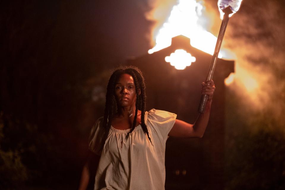 A woman holding a torch and a burning building behind her