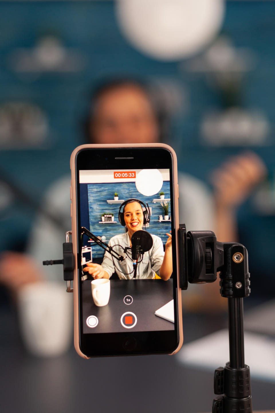 A person is being recorded on a smartphone while podcasting with a microphone and headphones