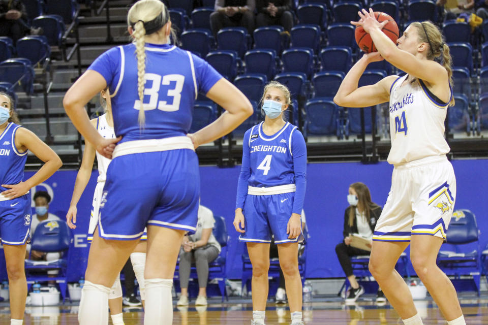 This photo provided by South Dakota State Athletics shows Creighton women's college basketball player Temi Carda (4), second from right, wearing a mask while an unidentified South Dakota State player shoots a free throw during an NCAA college basketball game in Brookings, South Dakota, Monday, Nov. 30, 3030. It's a common sight to see players and coaches wear masks on the sideline so far this season during college basketball games to help prevent the spread of the coronavirus. The DePaul and Creighton women's basketball teams are among a few squads that have taken it a step further with their players wearing the masks while they are on the court playing.(Christian Gravius/South Dakota State Athletics via AP)