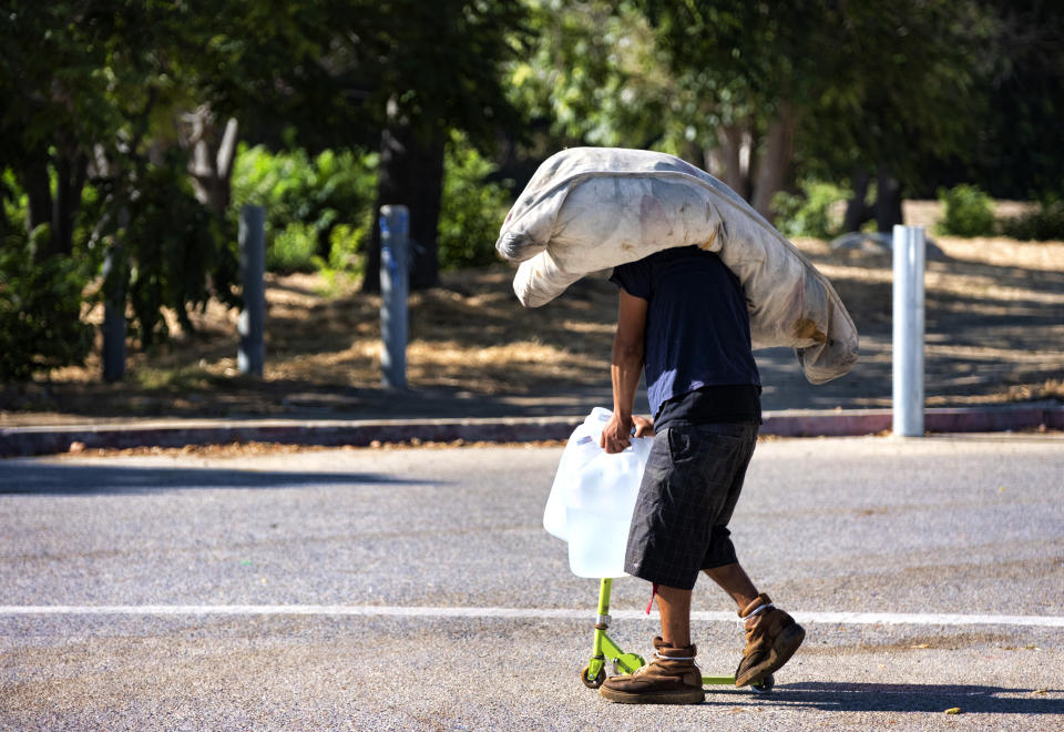 A homeless man struggles to haul his belongings and several large containers of water on his scooter in the San Fernando Valley section of Los Angeles, Tuesday, July 18, 2023. Forecasters have warned people of the extreme heat and that it can significantly increase the potential for heat-related illnesses, particularly for those working or participating in outdoor activities. (AP Photo/Richard Vogel)