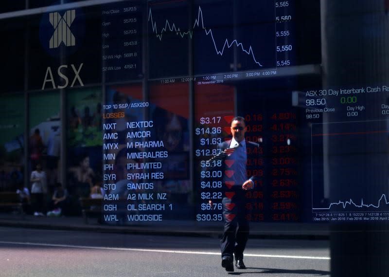 A pedestrian walks across a road and is reflected in a window displaying stock prices at the Australian Securities Exchange (ASX) in Sydney, Australia, November 28, 2016. REUTERS/Steven Saphore