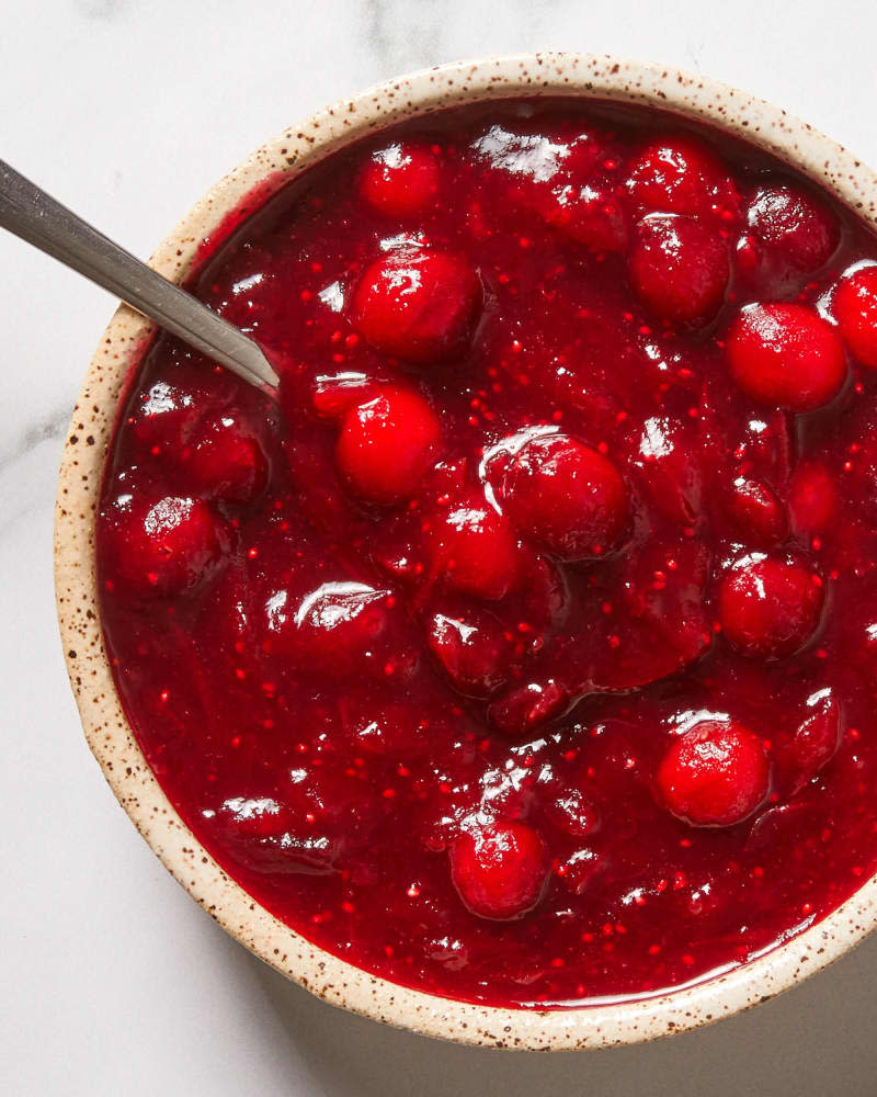 Overhead view of cranberry sauce in a white and brown speckled bowl with a spoon in the bowl.