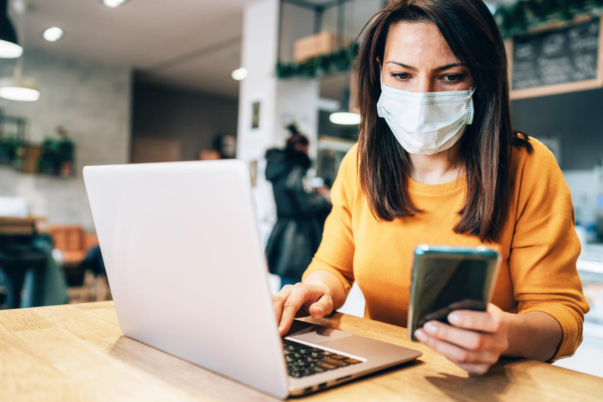 A woman uses a laptop at a cafe while wearing a face mask