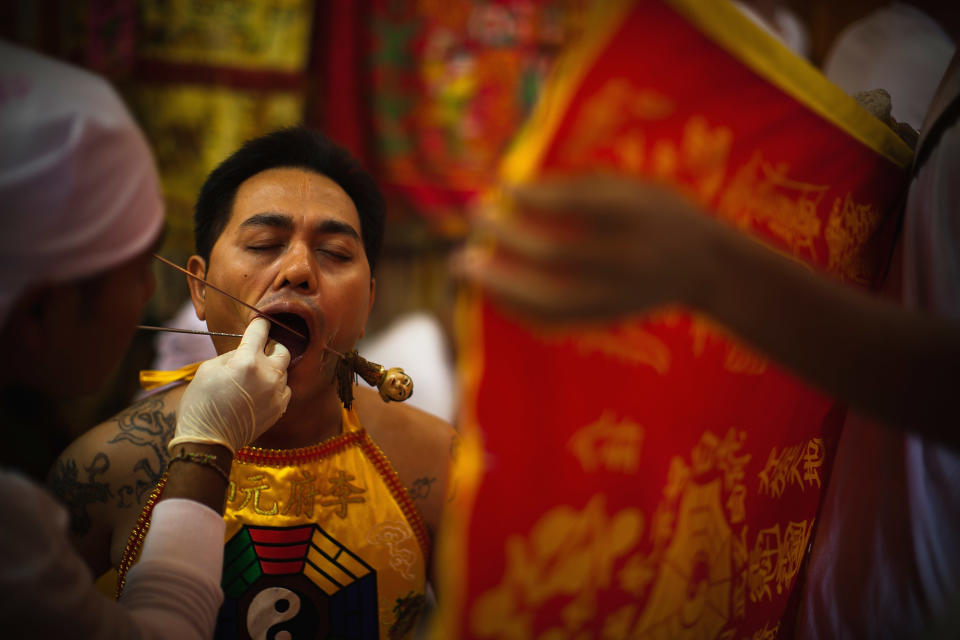 PHUKET, THAILAND - OCTOBER 05: A devotee of the Chinese shrine of Sui Boon Tong Shrine, pierces his cheeks with skewers during a procession of Vegetarian Festival on October 5, 2011 in Phuket, Thailand. Ritual Vegetarianism in Phuket Island traces it roots back to the early 1800's. The festival begins on the first evening of the ninth lunar month and lasts for nine days. Participants in the festival perform acts of body piercing as a means of shifting evil spirits from individuals onto themselves and bring the community good luck. (Photo by Athit Perawongmetha/Getty Images)