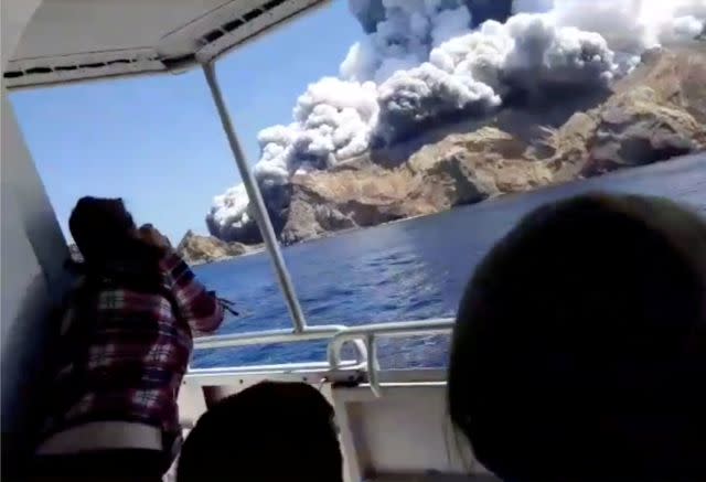 Tourists on a boat react as smoke billows from the eruption.