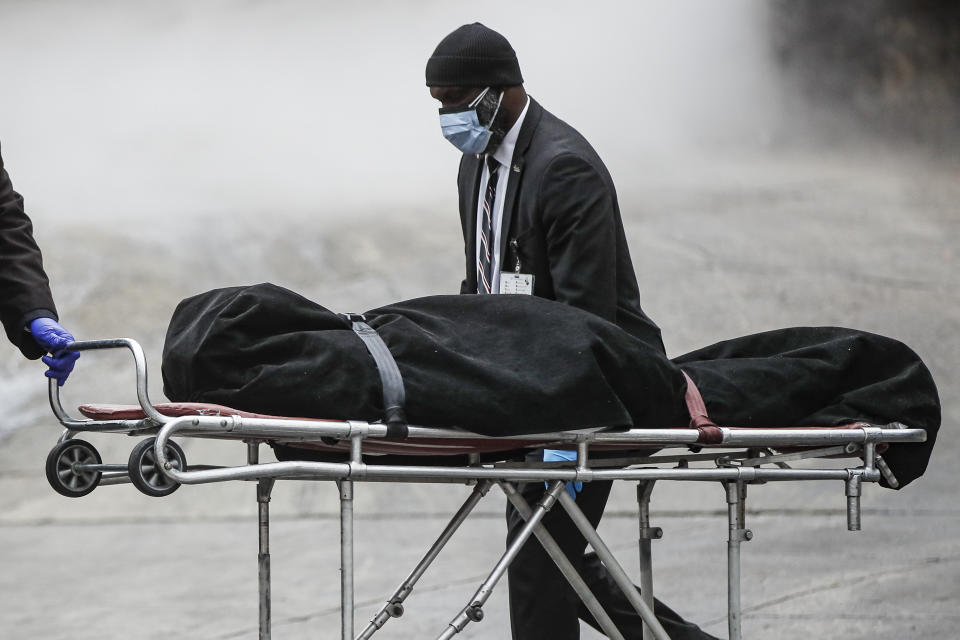 A hospital worker wears personal protective equipment due to COVID-19 concerns while moving bodies as a funeral director collects a body, Thursday, April 9, 2020, in the Brooklyn borough of New York. New York state posted a record-breaking number of coronavirus deaths for a third consecutive day even as a surge of patients in overwhelmed hospitals slowed, while isolation-weary residents were warned Thursday the crisis was far from over. (AP Photo/John Minchillo)