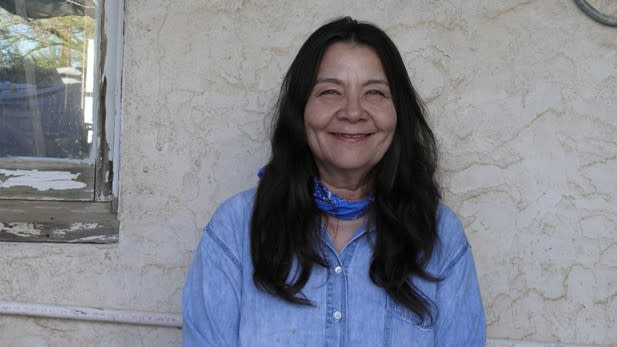 A woman stands against a house and smiles