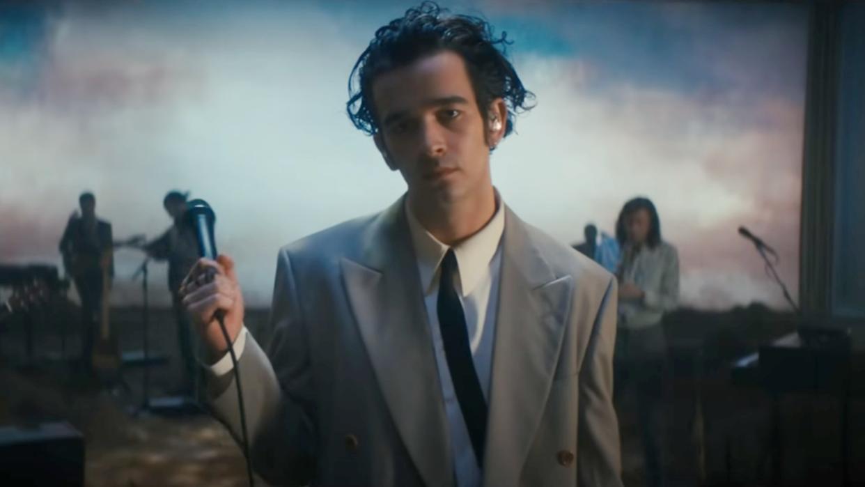  Matty Healy holding a mic in the Part of the Band performance by The 1975. 