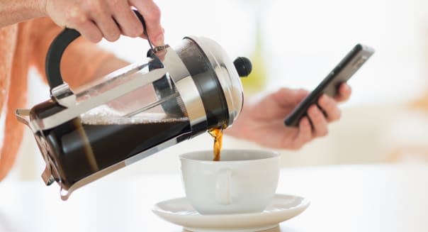 Close-up of woman pouring coffee and looking at phone