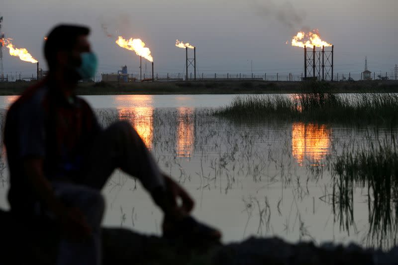 FILE PHOTO: Flames emerge from flare stacks at Nahr Bin Umar oil field, as a man is seen wearing a protective face mask , following the outbreak of the coronavirus, north of Basra