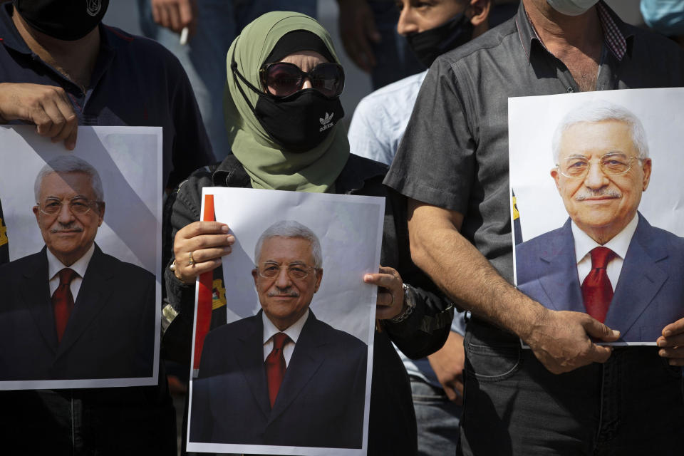 FILE - In this Sept. 27, 2020 file photo, Palestinians wearing protective face masks amid the coronavirus pandemic, hold pictures of Palestinian President Mahmoud Abbas during a rally to support Abbas, in the West Bank town of Tubas. President Abbas called for legislative elections on May 22 and presidential elections on July 31, 2021. (AP Photo/Majdi Mohammed, File)