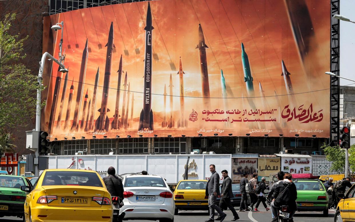 Motorists drive their vehicles past a billboard depicting named Iranian ballistic missiles in service, with text in Arabic reading "the honest [person's] promise" and in Persian "Israel is weaker than a spider's web"