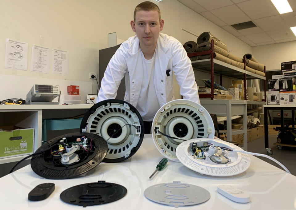 Man looks at camera while standing in lab with two dismantled fans. 