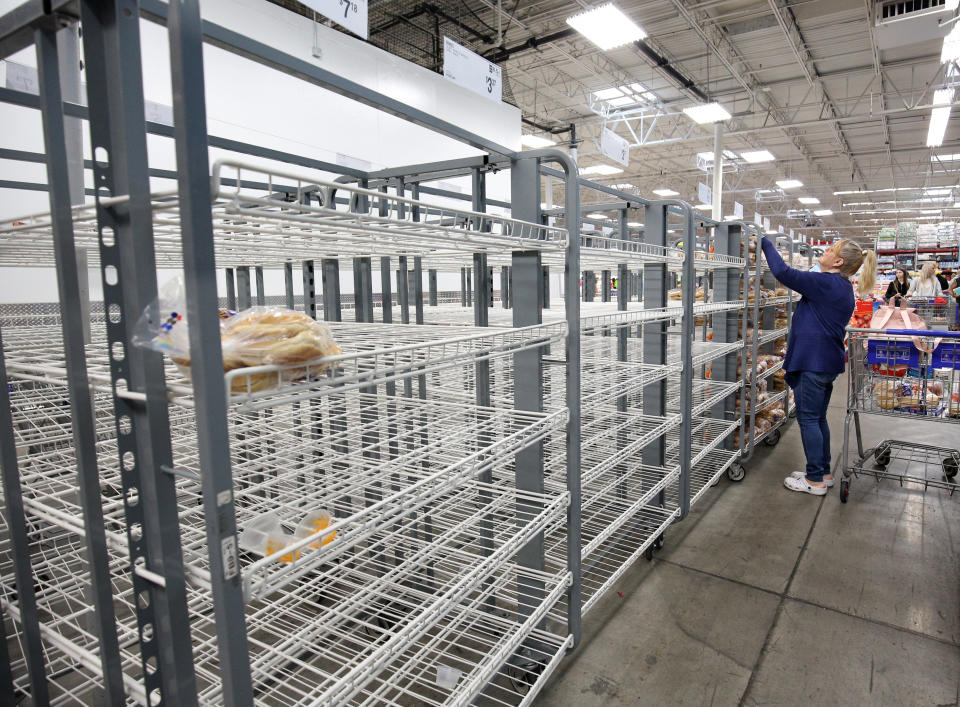 Person shopping in a supermarket with mostly empty metal shelves, reaching for remaining bread