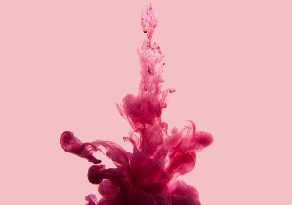 Pink paint swirling in the water, creating abstract, complex shapes against a simple background