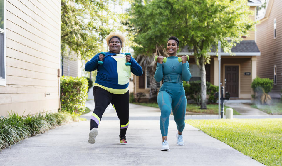 Two individuals exercising outdoors, one using a resistance band, both in athletic wear