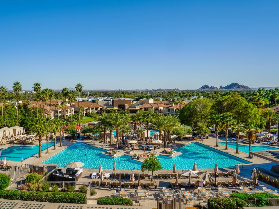 A resort with pools and palm trees in front of a mountain with blue skies in the background