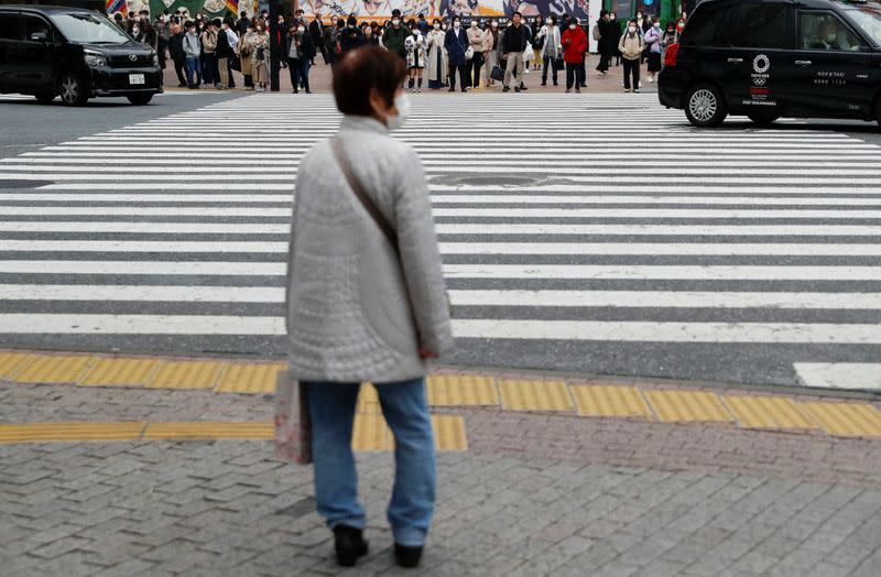 Pedestrians wearing protective face masks, following an outbreak of the coronavirus disease, wait for changing traffic signal at Shibuya Crossing in Tokyo, Japan