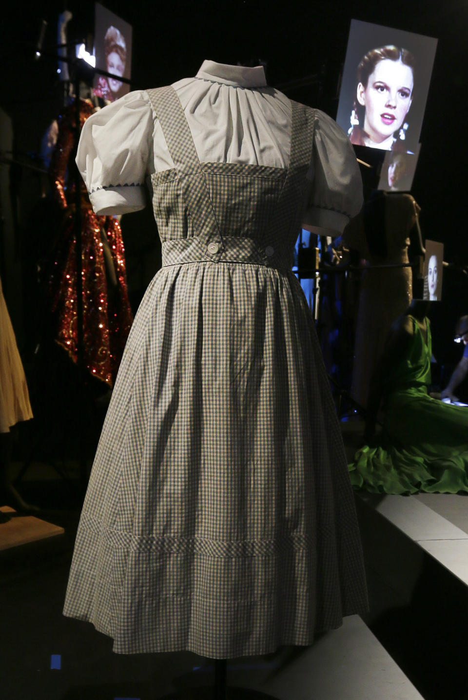 In this Tuesday, Oct. 16, 2012 photo, the blue-and-white gingham pinafore dress worn by Judy Garland in her iconic role of Dorothy designed by Adrian for the 1939 film "The Wizard Of Oz," with a video portrait of garland in the background, appears on display at the Hollywood Costume exhibition at the Victoria and Albert museum in London. On Sunday, Nov. 11, 2012, auction house Julien's Auctions said the gingham dress fetched the highest price of any item during a two-day auction of Hollywood memorabilia that attracted bids from around the world, selling for $480,000. (AP Photo/Alastair Grant)