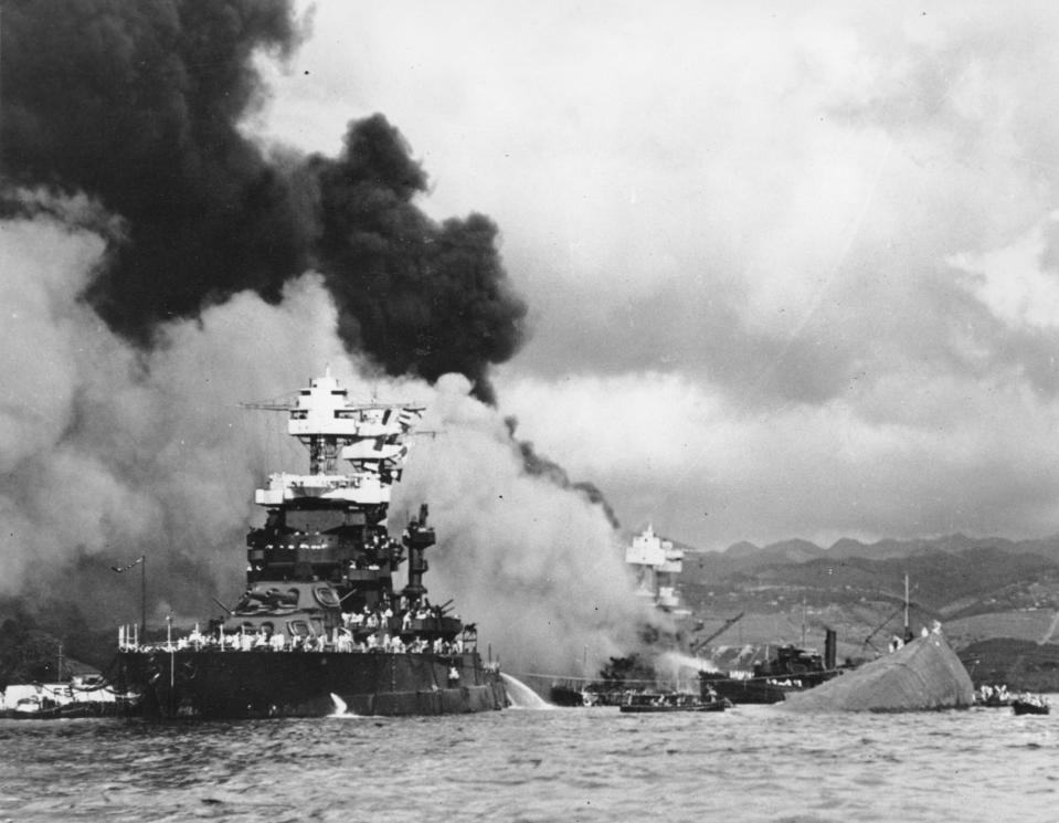 The hull of the capsized USS Oklahoma is seen at right as the battleship USS West Virginia, center, begins to sink after suffering heavy damage, while the USS Maryland, left, is still afloat in Pearl Harbor, Hawaii.