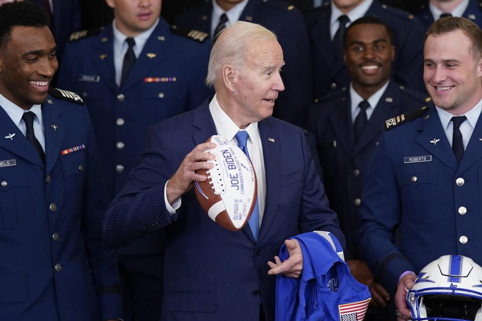 Air Force quarterback Haaziq Daniels, left, and Air Force running back Brad Roberts, right, look on as President Joe Biden holds a football during an event to present the Commander-in-Chief's trophy to the Air Force Academy in the East Room of the White House, Friday, April 28, 2023, in Washington. (AP Photo/Evan Vucci)