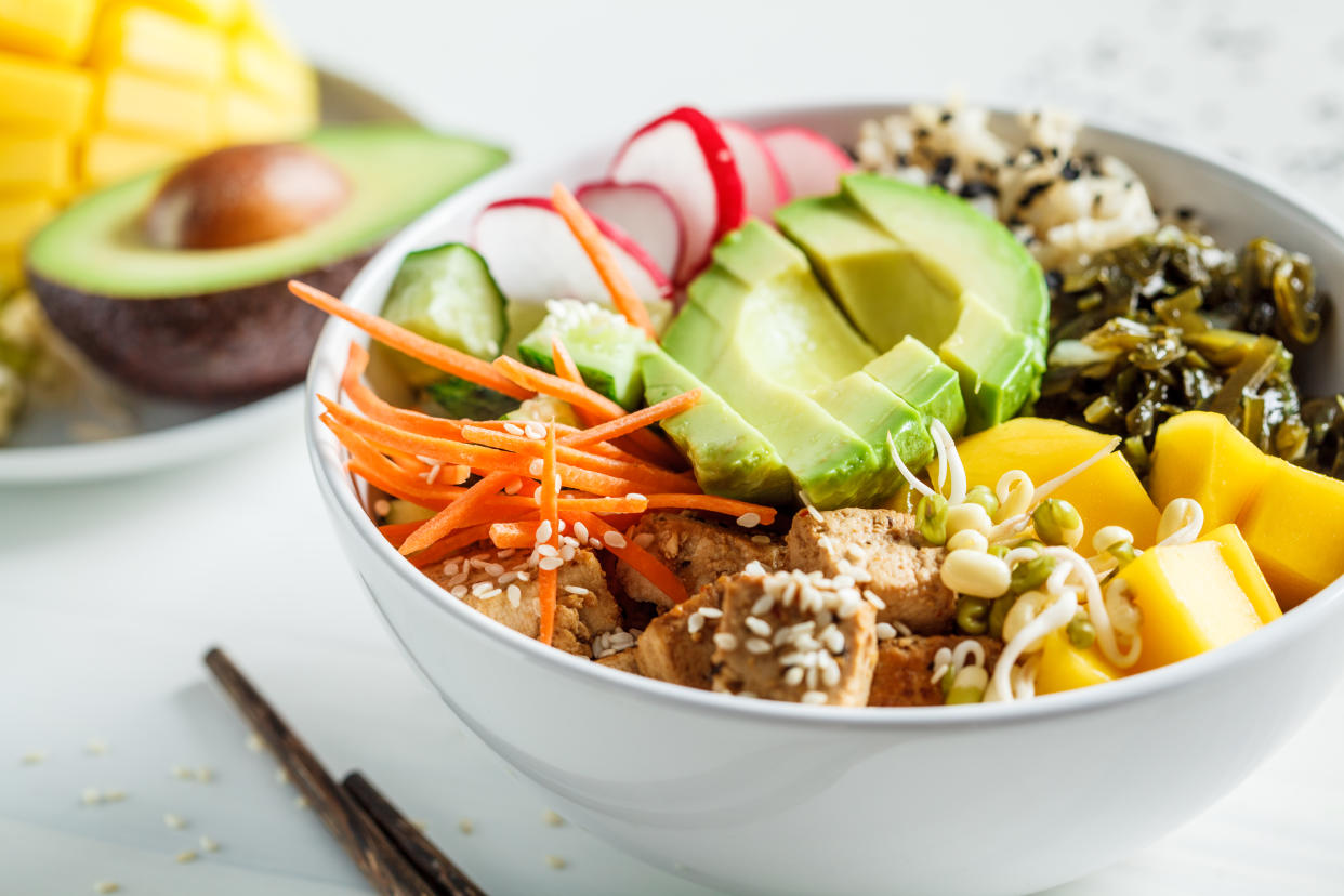 Vegan poke bowl with avocado, tofu, rice, seaweed, carrots and mangoes, white background. Vegan food concept.